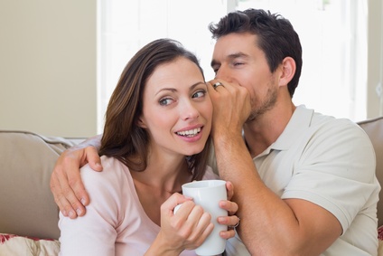 Man whispering secret into a happy womans ear in living room