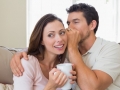 Man whispering secret into a happy womans ear in living room